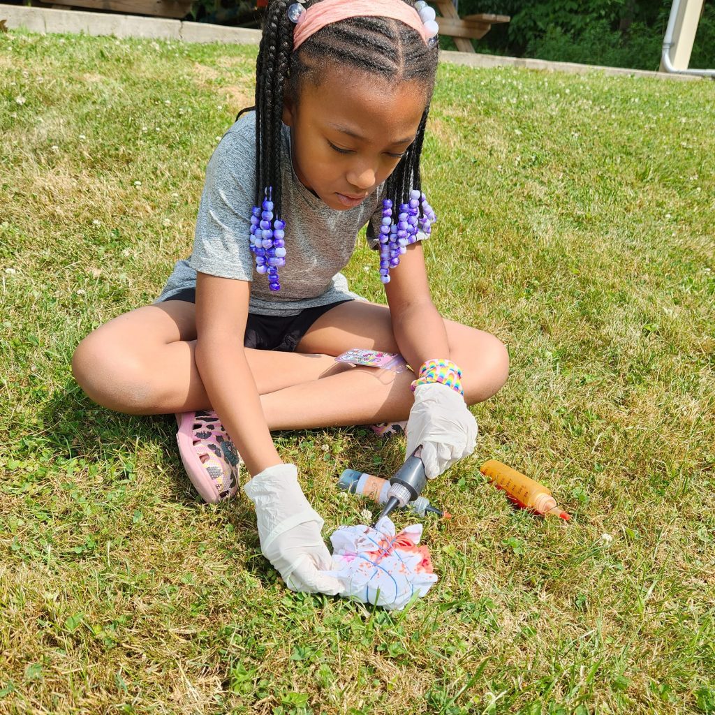 Young girl sits on grass creating a tie die shirt