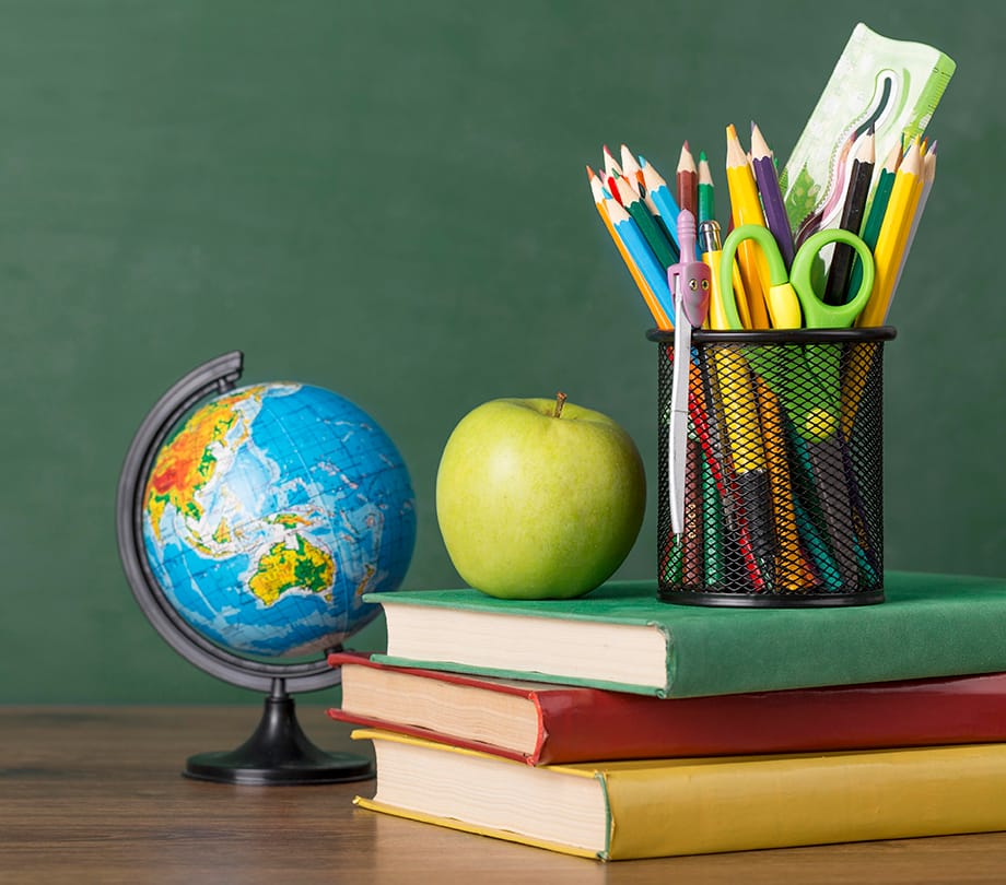 A stack of three books, a globe, apple and other school supplies on a desk.