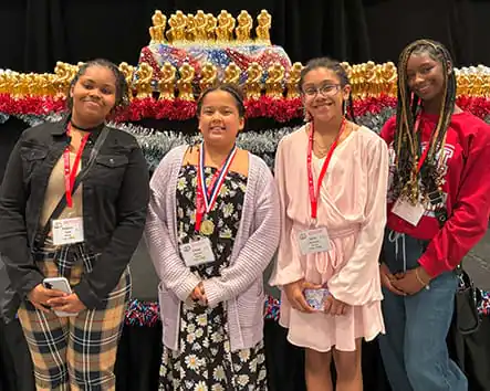 Four females student pose in front of gold trophies. Four females student pose in front of gold trophies.