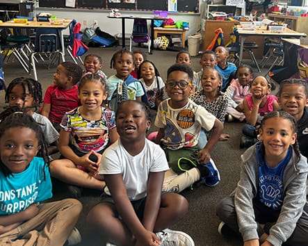A classroom with kids sitting on the floor.