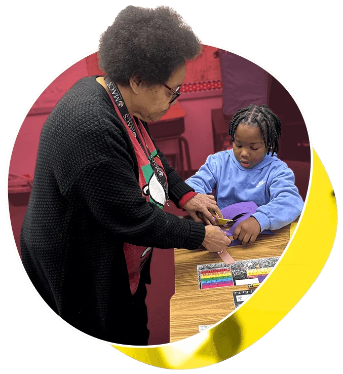 A teacher works with a young male student at his desk.