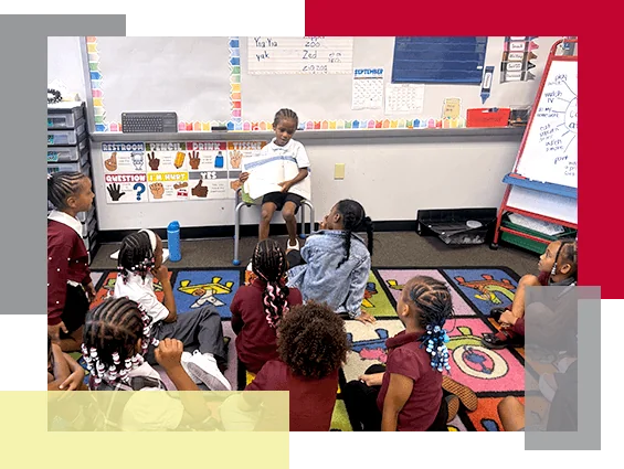 A boy sitting in a chair reads to group of students.